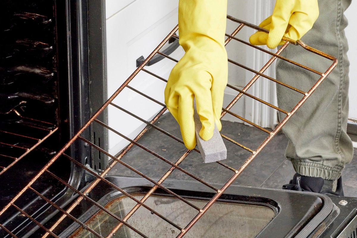 DIYer using a pumice stone to remove baked on gunk from oven grates.