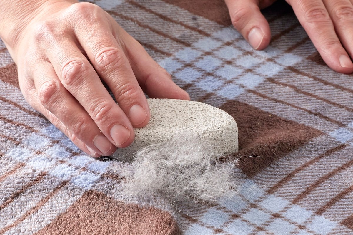 A DIYer using a pumice stone to life pet hair off of a blanket. 