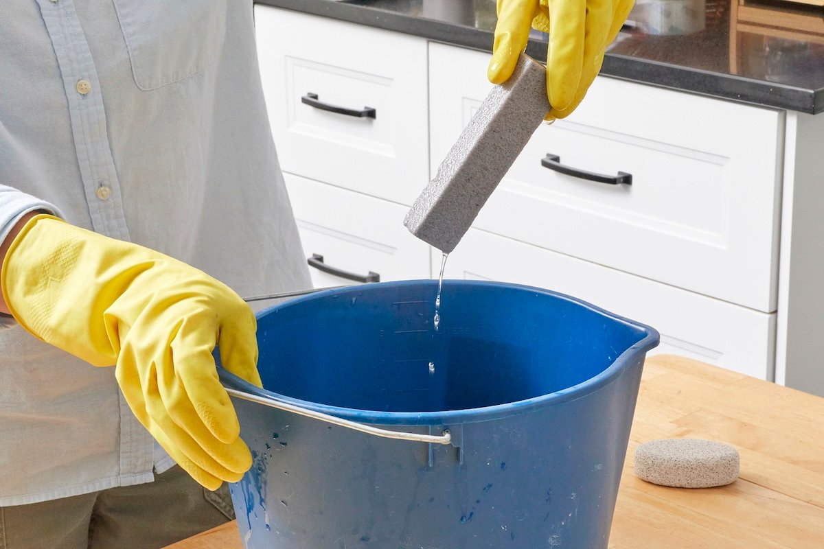 A DIYer dipping a pumice stone into water before using it to clean the kitchen.
