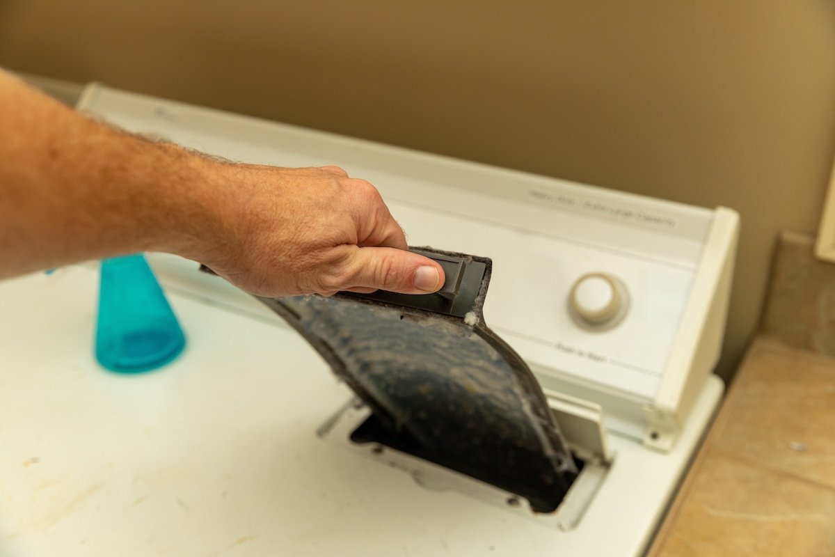 A person pulls the lint trap from a front-loading dryer out to clean it.