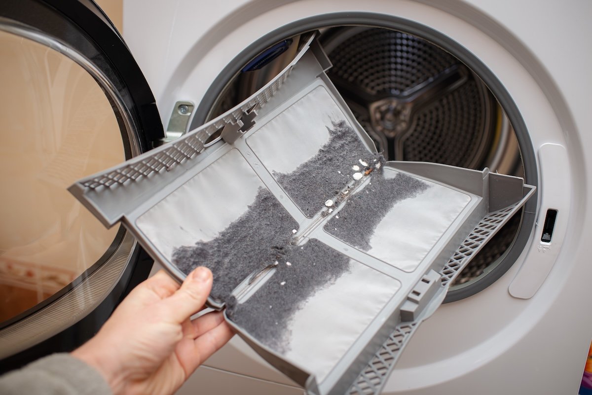A person removes a folding lint trap from a dryer. 