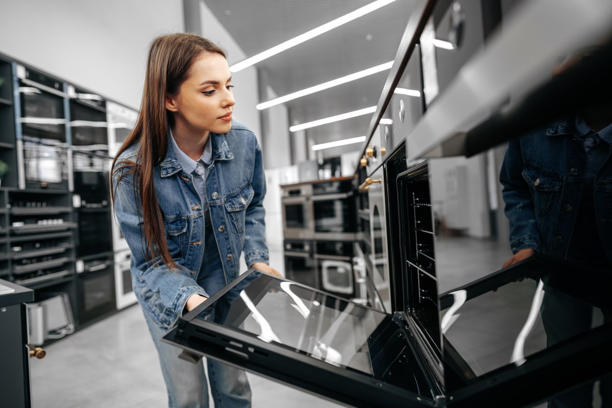 Young woman with long hair shopping for an electric oven opens the oven door.