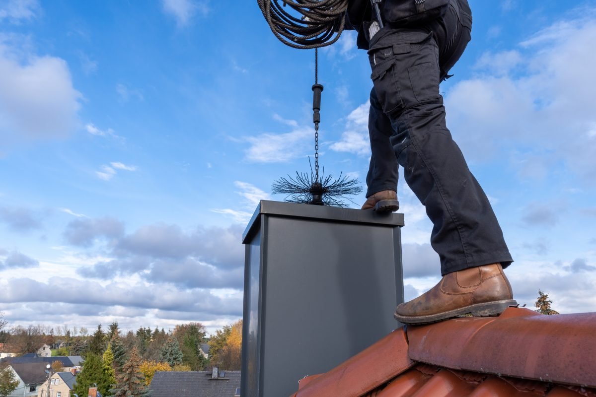 Chimney sweep cleaning a chimney standing on the house roof, lowering equipment down the flue
