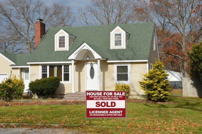House with chimney that has a For Sale sign in the front yard