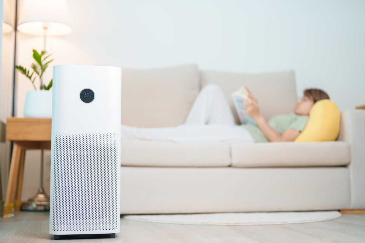 Air purifier in the foreground with a woman reading and relaxing on a sofa.