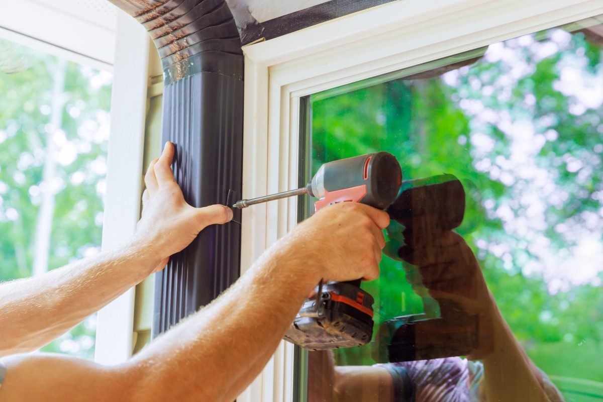Man is assembling gutter channel that is attached to roof with installation of gutter.