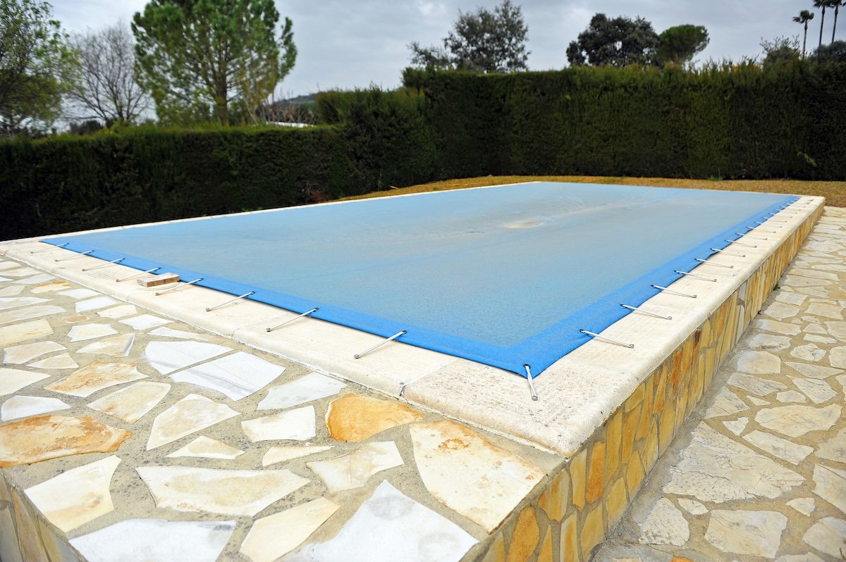 Swimming pool protected by a blue tarrp during the winter.