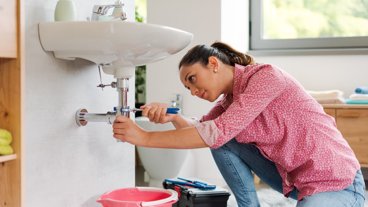 Skilled young woman fixing the bathroom sink by herself using water pump pliers, DIY concept