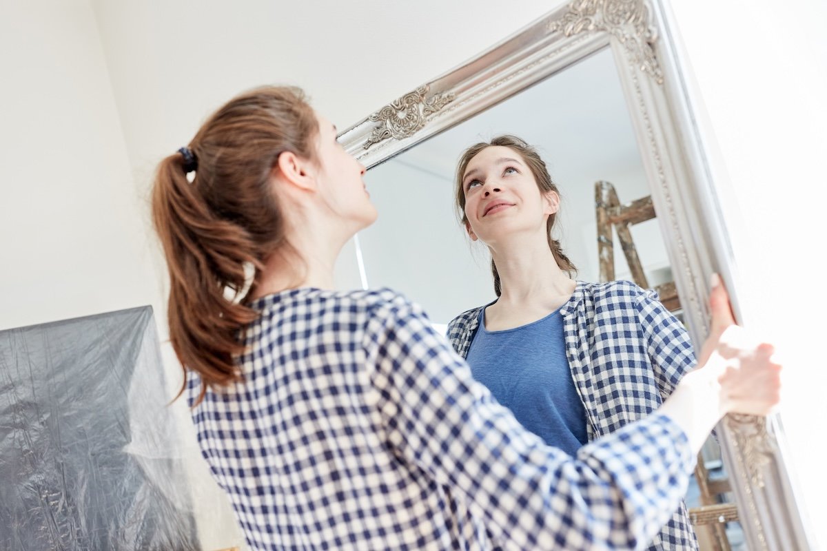 Young woman hangs a mirror on the wall in her new apartment.