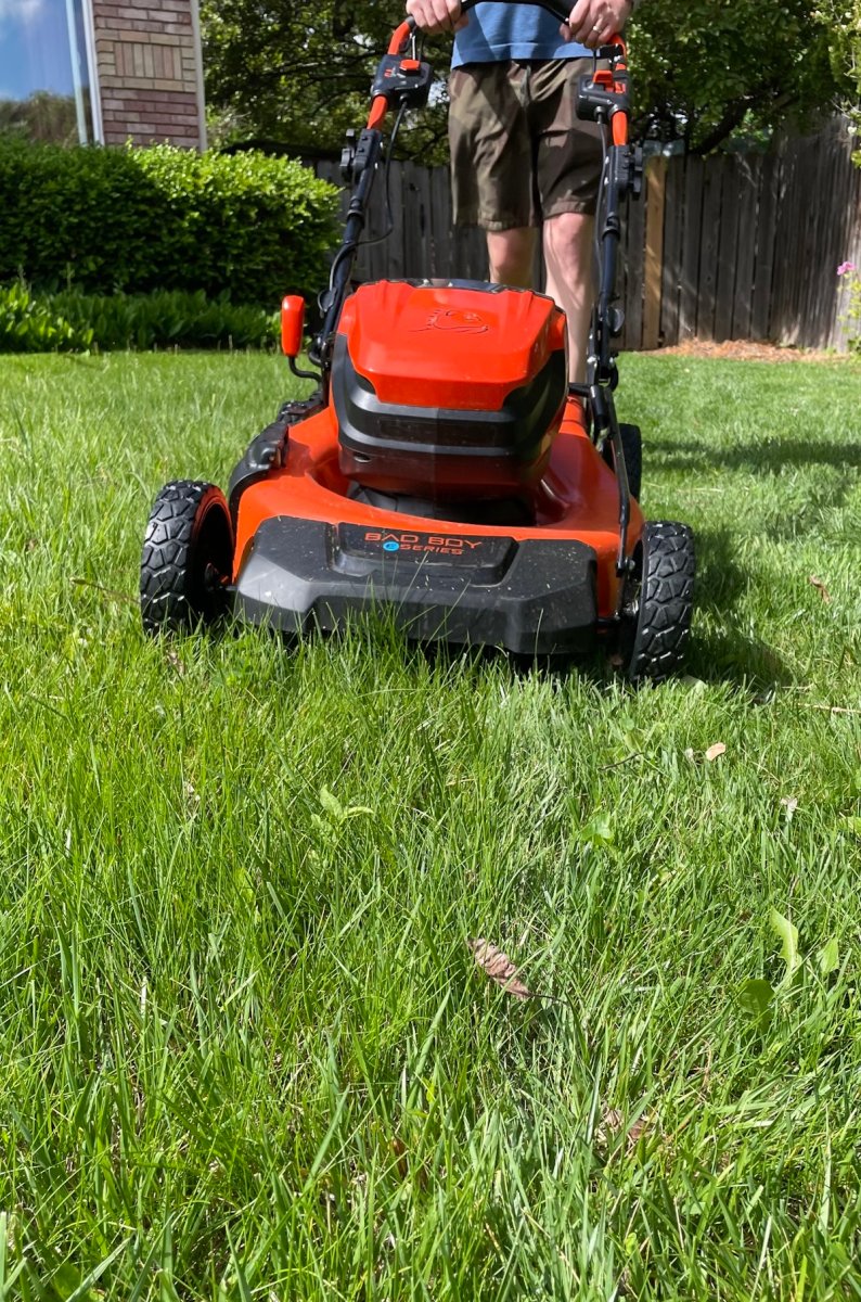 Person pushes a red mulching lawn mower across a grassy property.