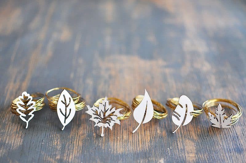 Six golden handmade DIY fall-themed napkin rings laid out on a table.