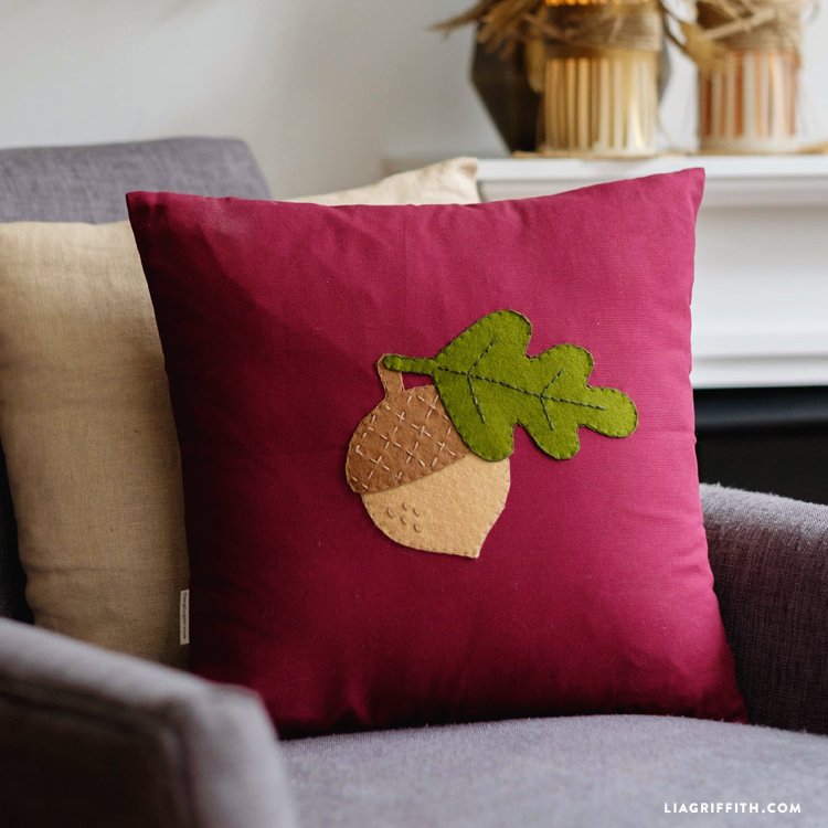 Burgundy throw pillow with an appliqued acorn and leaf.