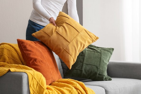 Woman arranging decorative pillows in fall colors on a modern sofa.