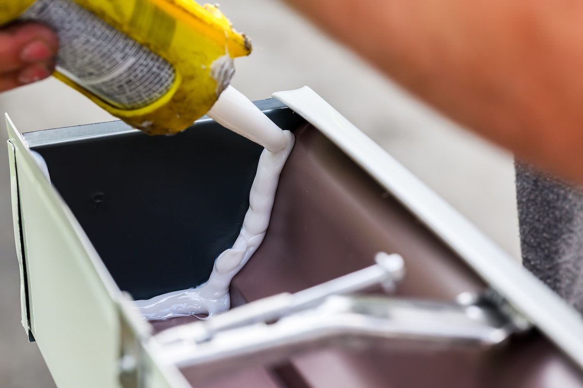 Person uses caulk to seal insides of rain gutters.