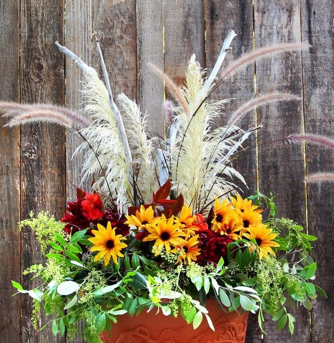 A large terracotta planter with fall flowers and tall ornamental grass.