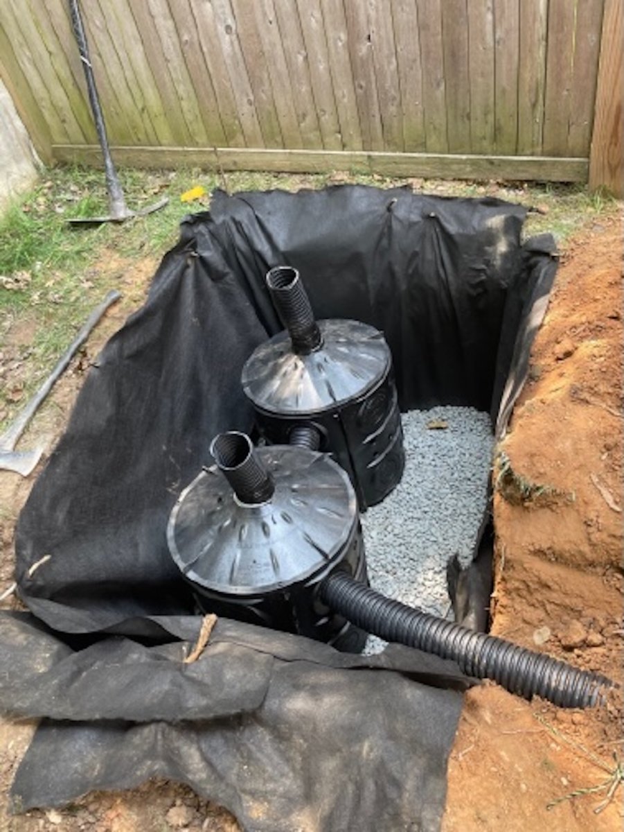 Two barrels being built into a ground pit to create a dry well. 