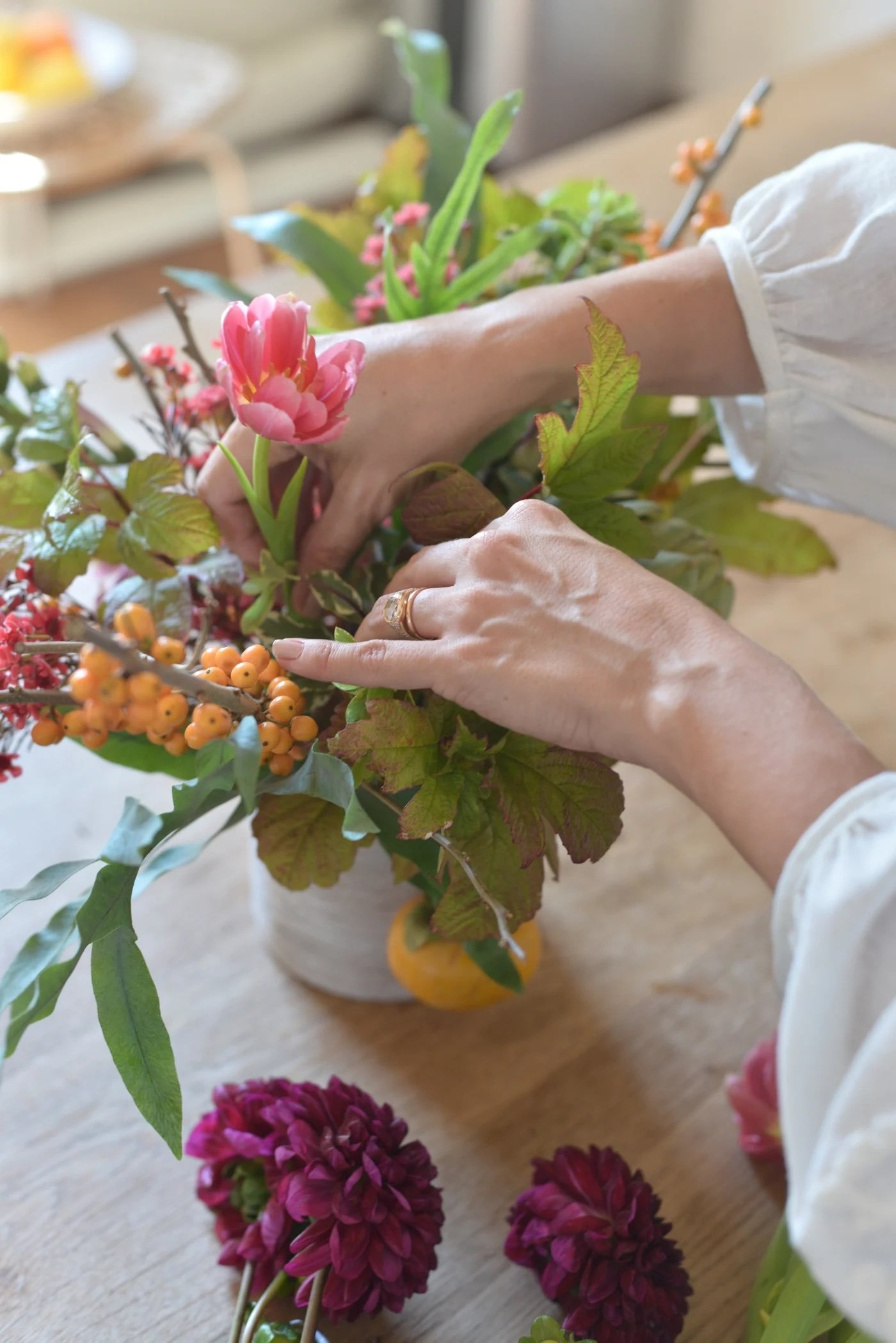 View of woman's hands arranging fall flowers in a vase.