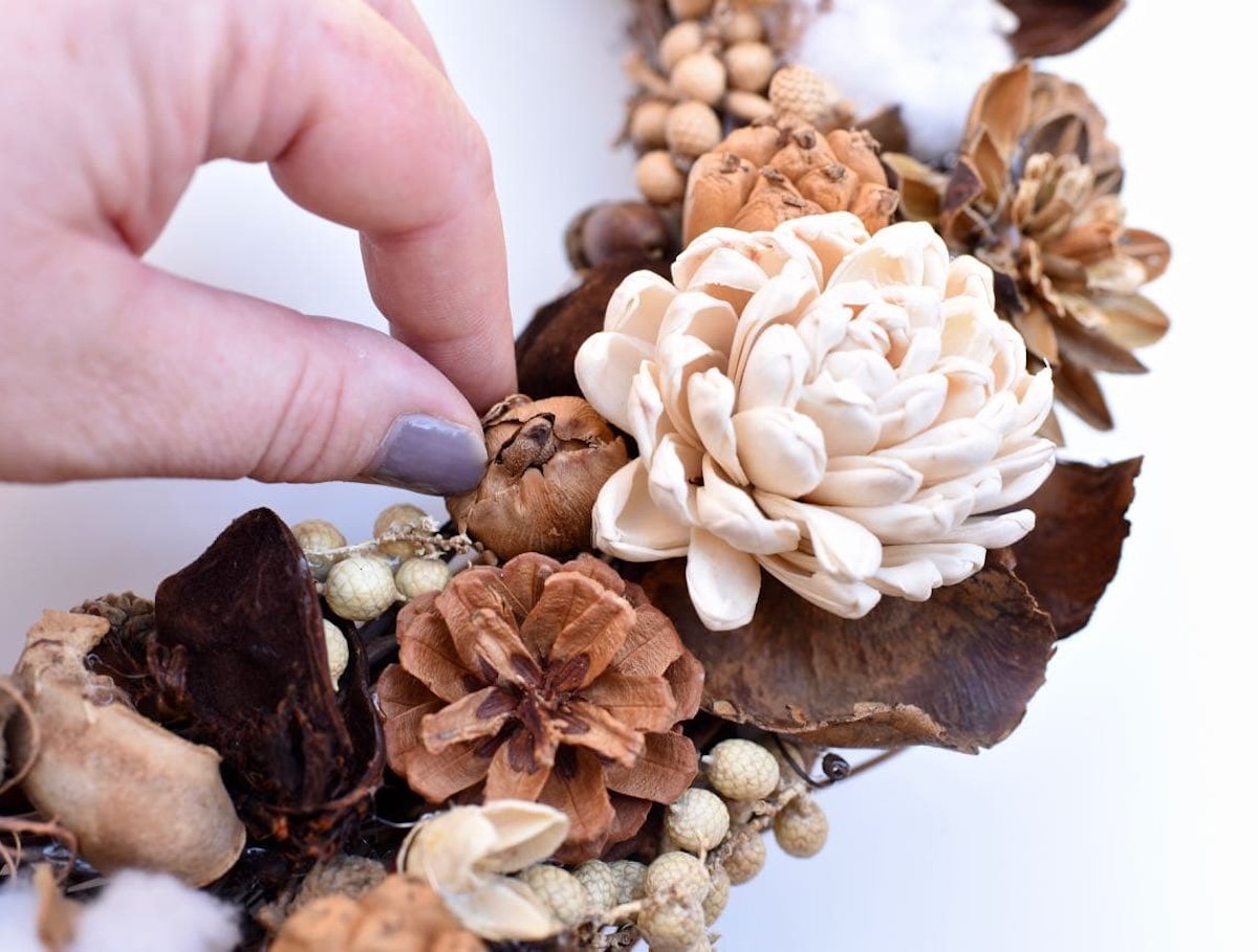 Closeup of a woman's hands placing dried flowers on a grapevine wreath.
