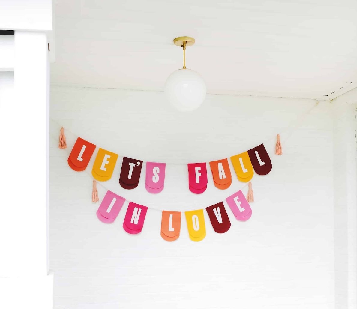 A colorful banner with "let's fall in love" spelled out hangs on a white wall.