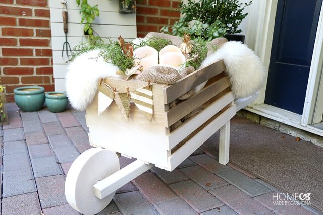 Painted white wooden wheelbarrow filled with fall greenery on an outdoor patio.