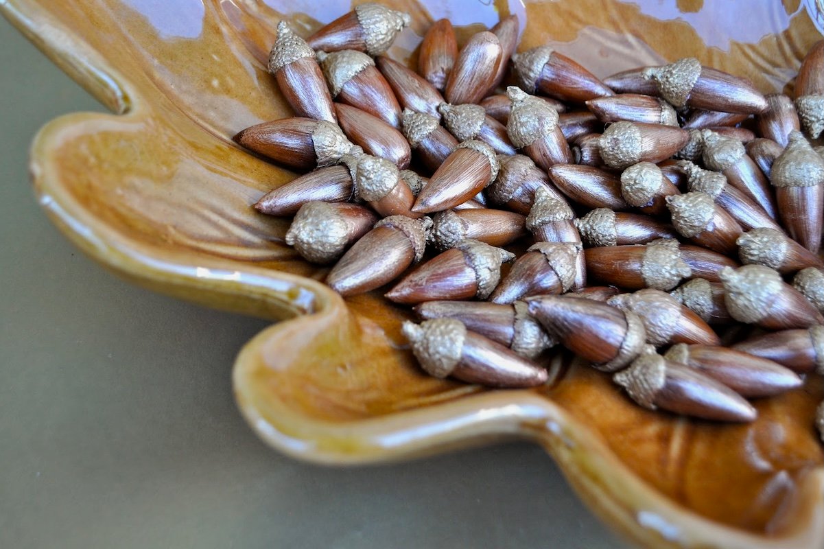 Acorns that have been gilded with metallic paint are gathered on a leaf-shaped plate.