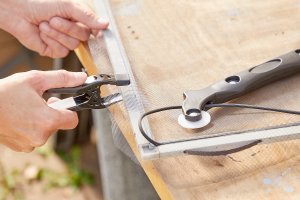 Woman clamps window screening to the frame to prepare to install the spline.