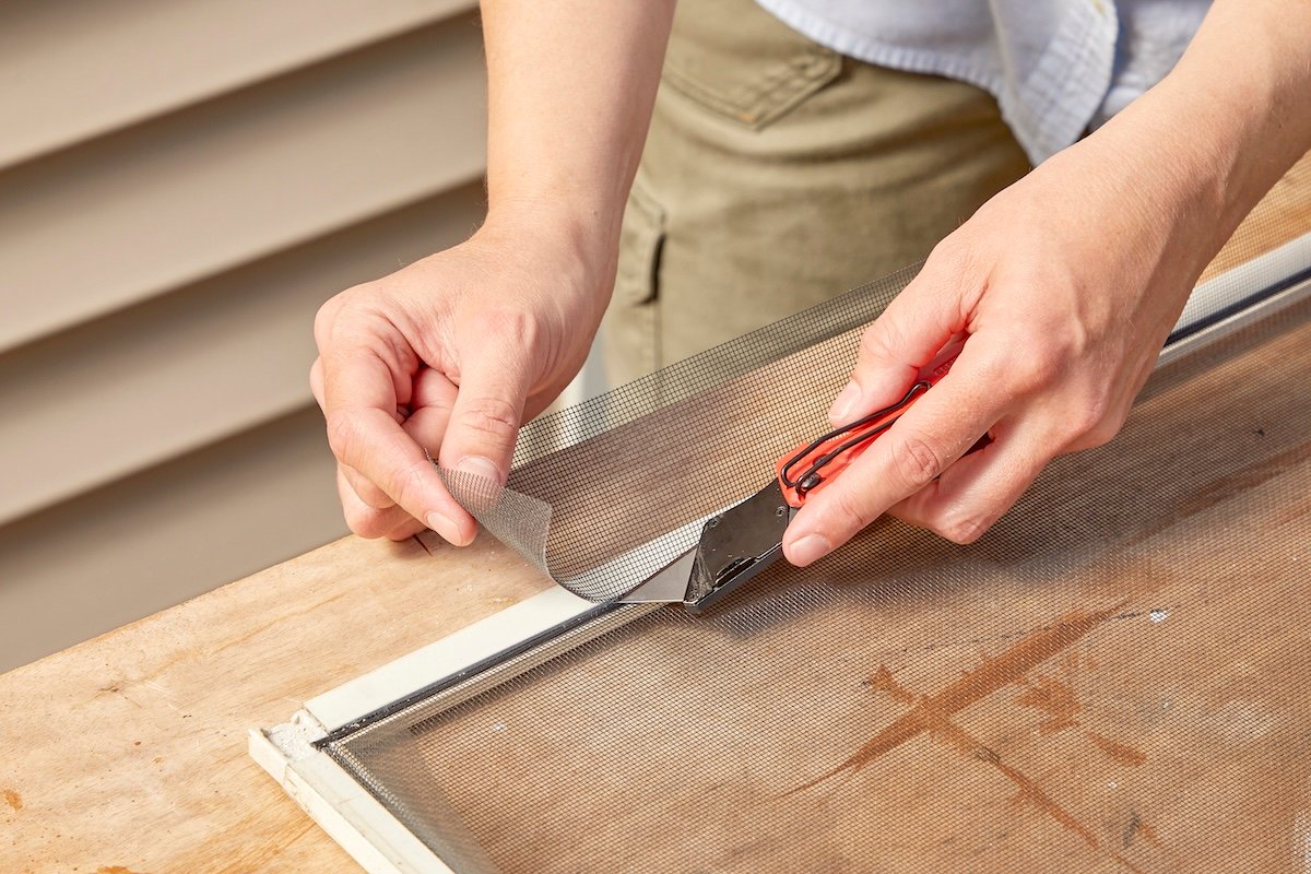 Woman cuts excess screen after replacing window screen and spline.