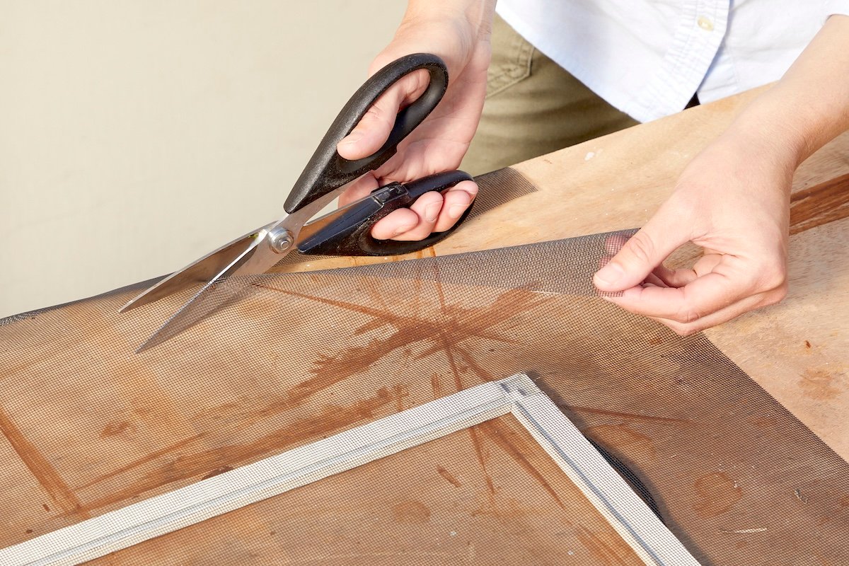 Woman uses scissors to cut window screening to fit closer to window frame.