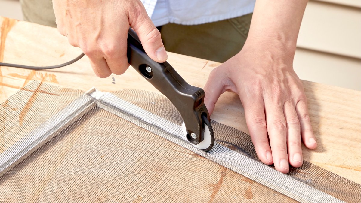 Woman uses a spline tool to replace the material in a window screen.