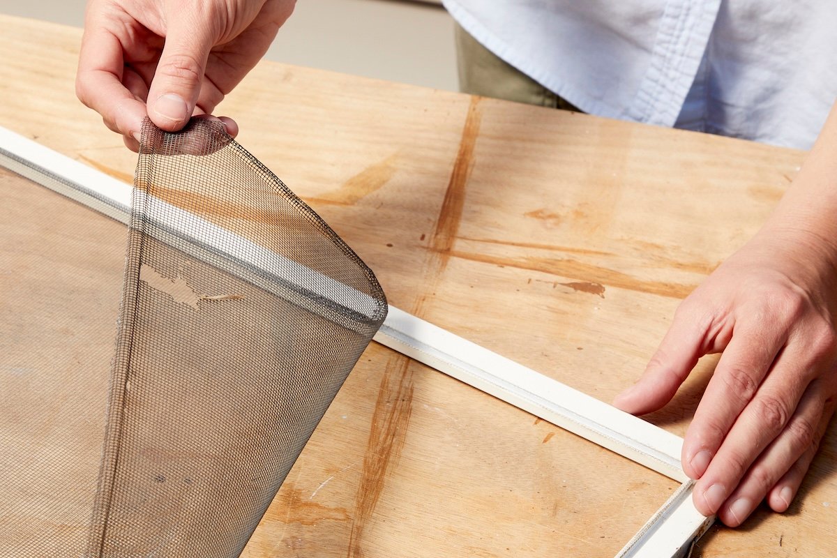 Woman removes a torn window screen from its frame.
