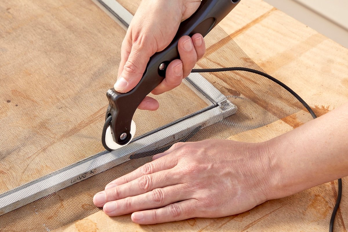 Woman uses a spline wheel to push spline into window screen channel.