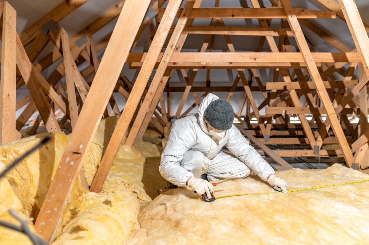 Man in beanie cap and white coat insulating the attic with glass wool.