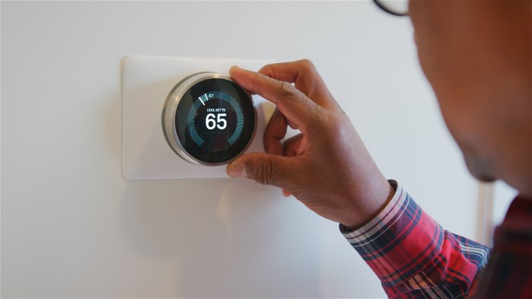 Man adjusting smart thermostat on the wall with his hands.