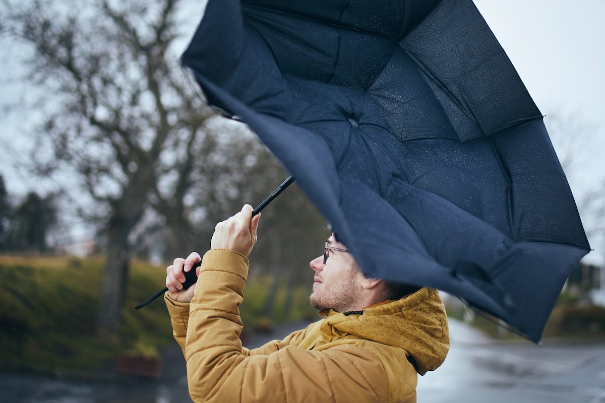 Man holding broken umbrella in strong wind during gloomy rainy day. T