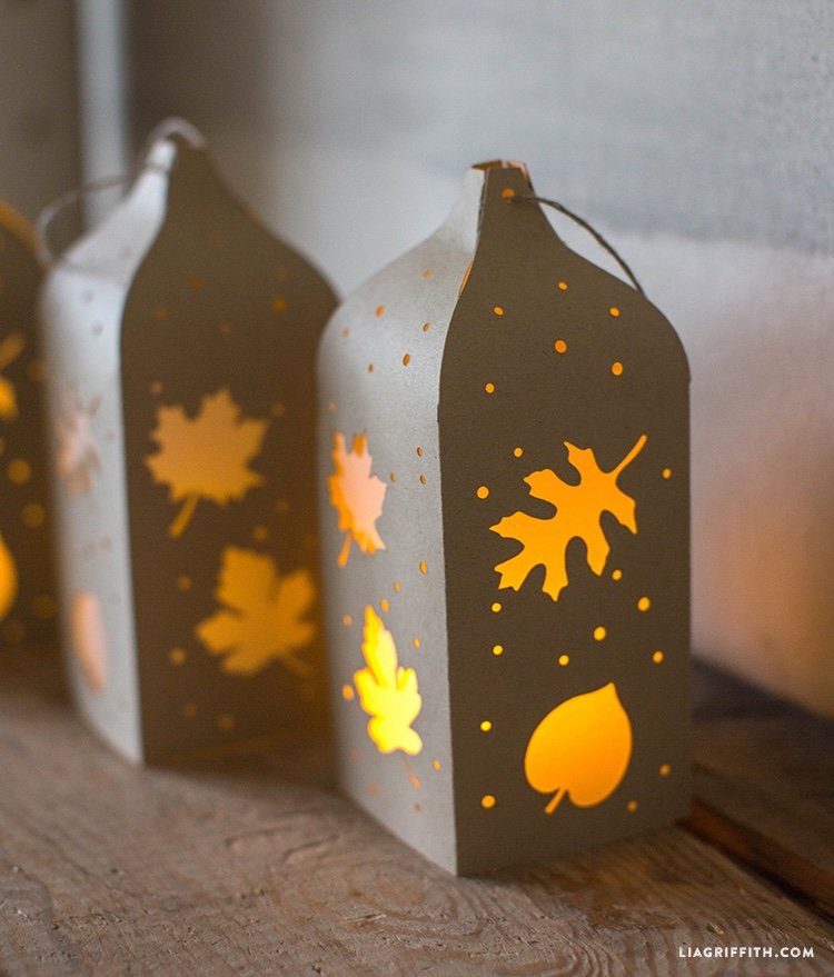 Illuminated, metallic-colored paper lanterns with fall-themed cutouts.
