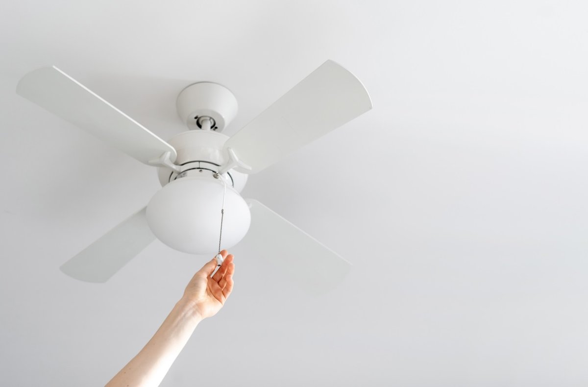 cropped shot of female hand pull switch of ceiling fan with lamp on white background with copy space, room cooling and ventilation concept
