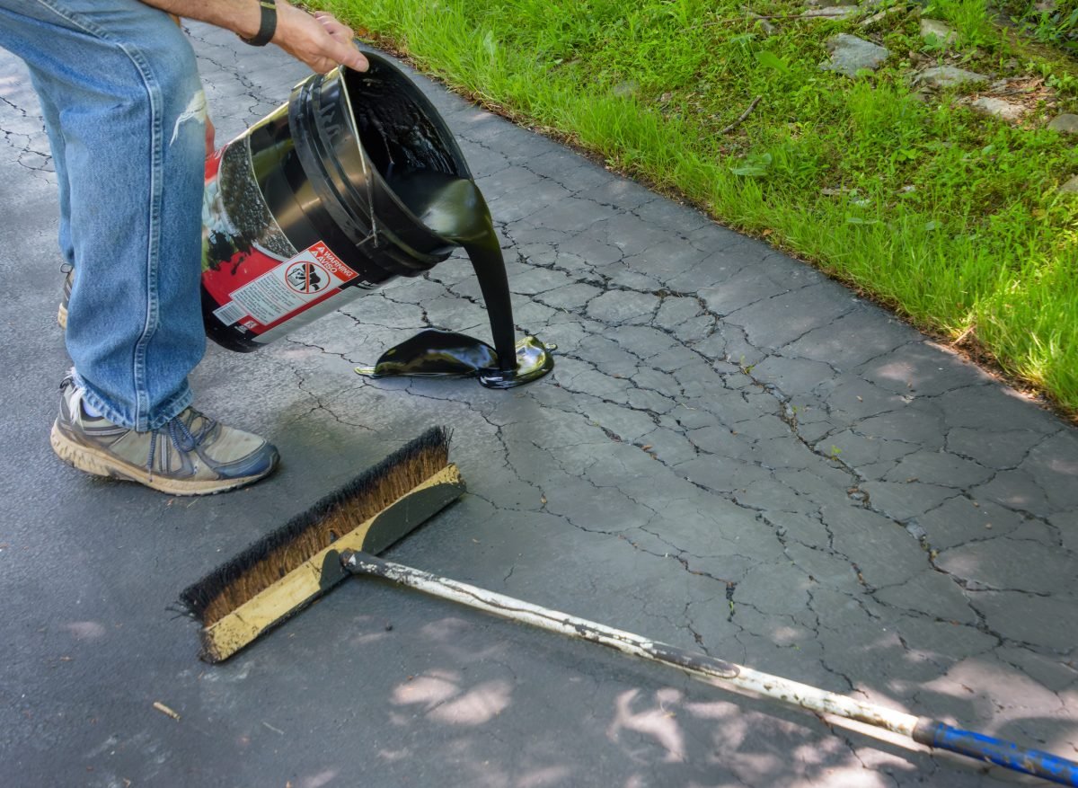 Man pouring asphalt sealant on driveway to repair cracks.