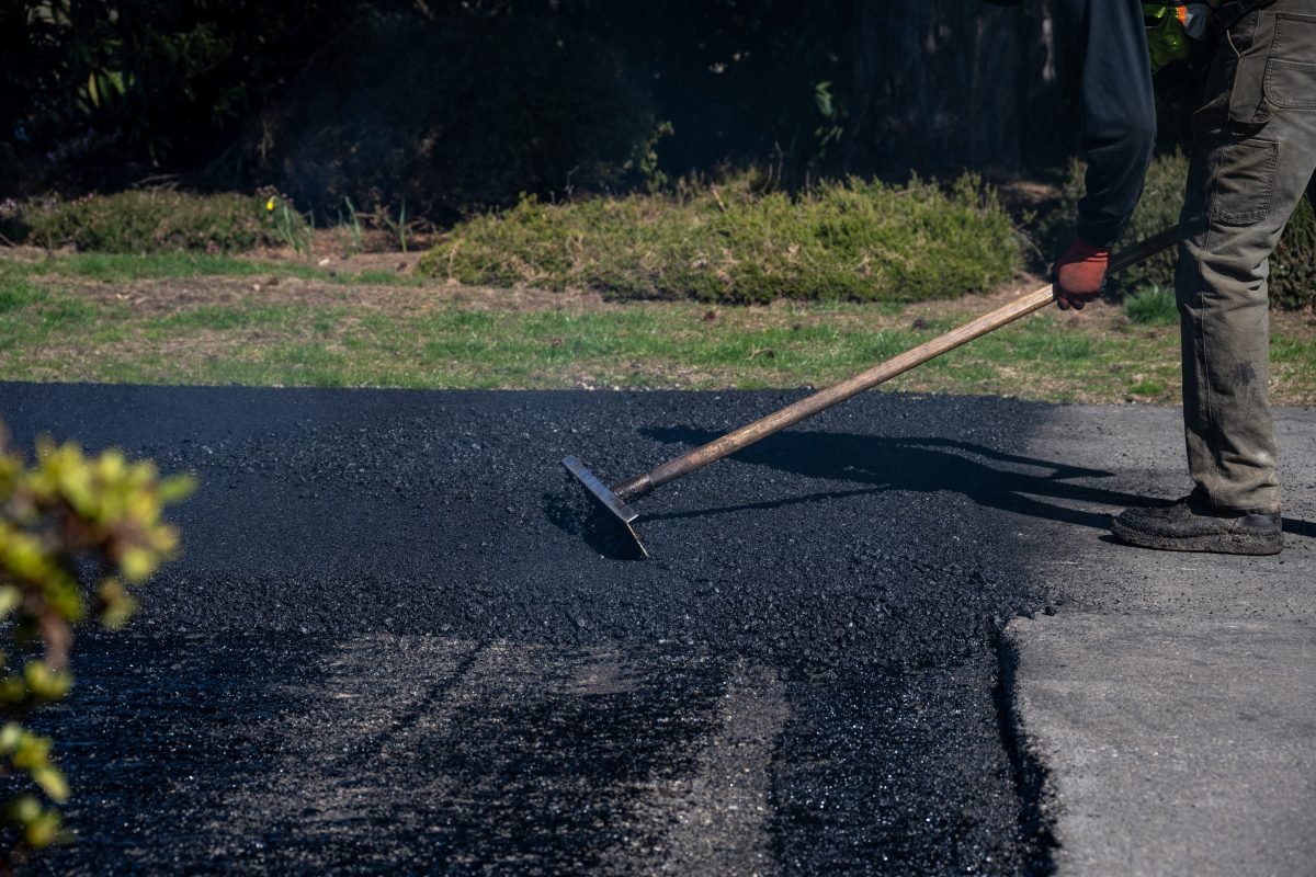 Construction worker with asphalt rake smoothing out fresh blacktop on driveway