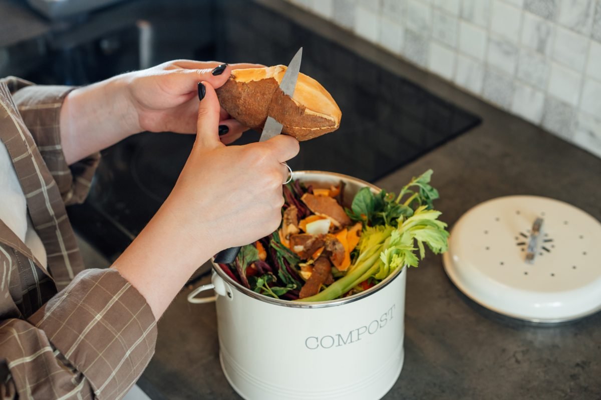 Woman putting cut vegetable waste into a compost bin