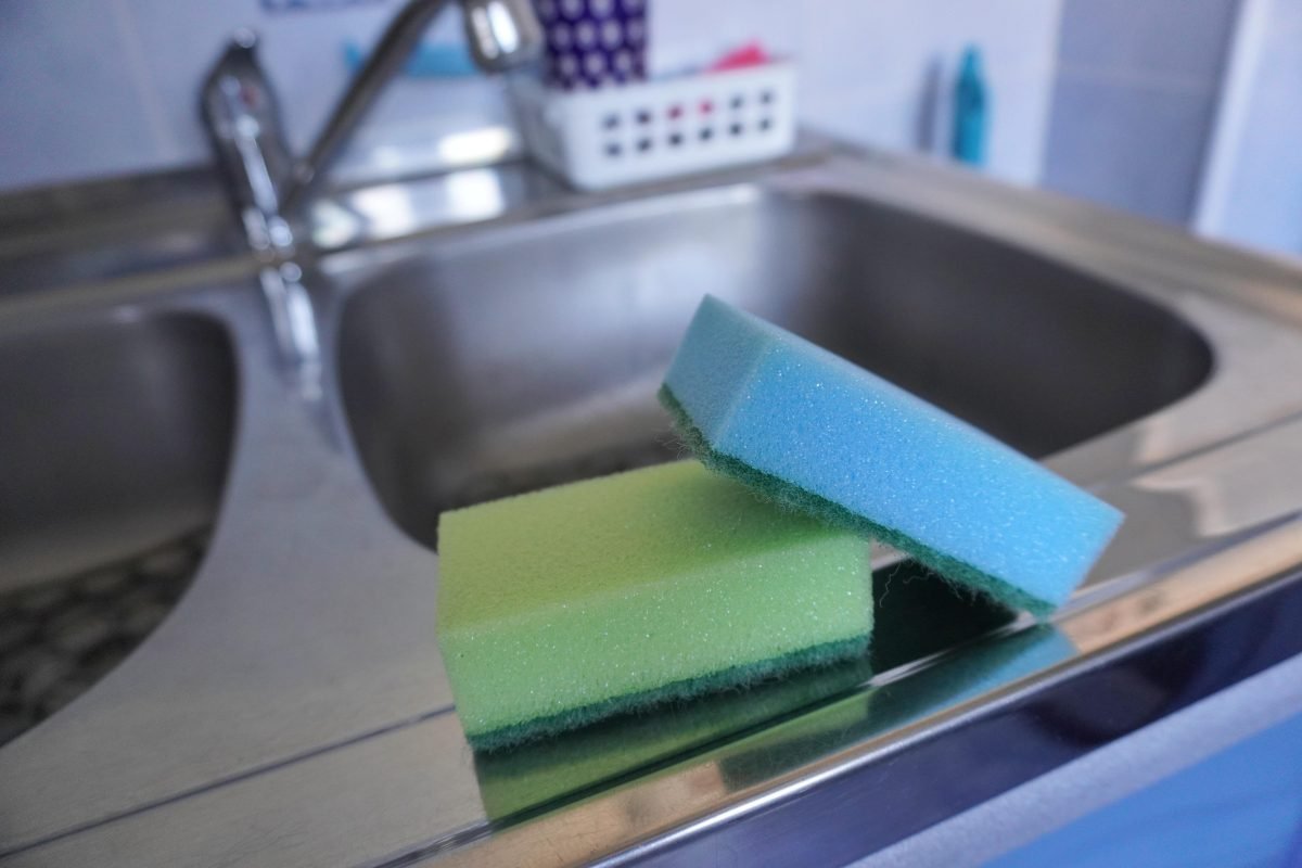Two scouring sponges stacked on a shiny stainless steel kitchen sink edge