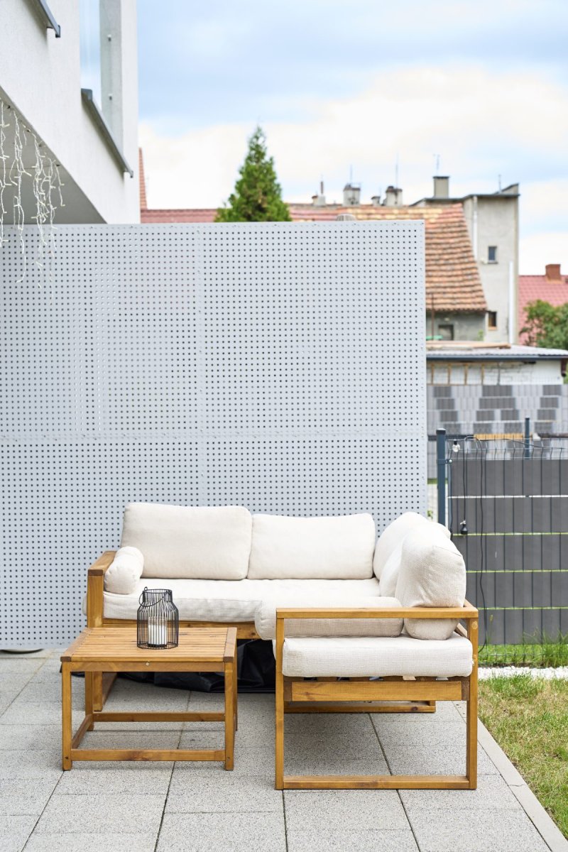 Wooden patio sofa, chair and table arranged beside perforated privacy screen.