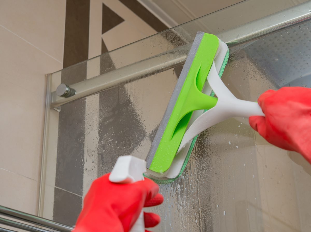 Hand cleaning glass shower doors wtih a spray and squeegee