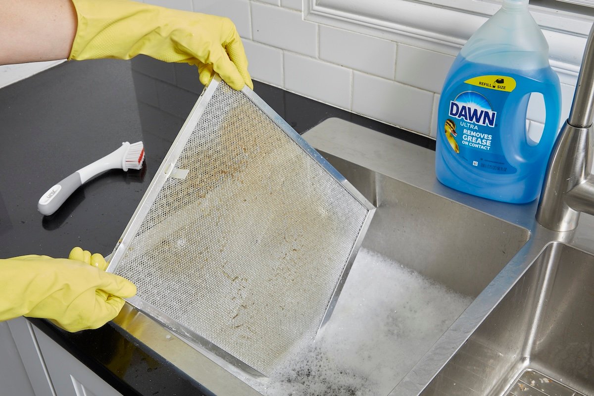 A DIYer soaking a range hood filter in a kitchen sink with dish soap.