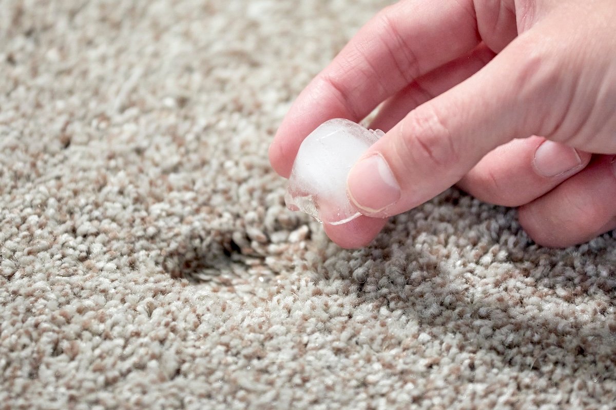Woman holds ice cube over a dent in beige carpet.