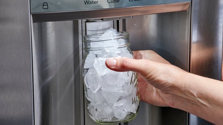 Woman collects ice from ice maker using a Mason jar.