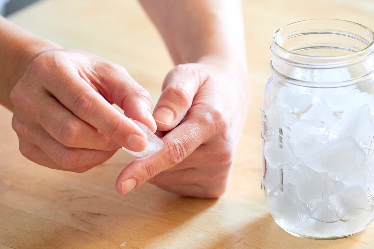 Woman with a jar of ice presses an ice cube against her finger.