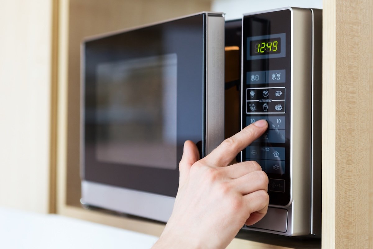 Close up of a male hand pushing a button on a microwave.