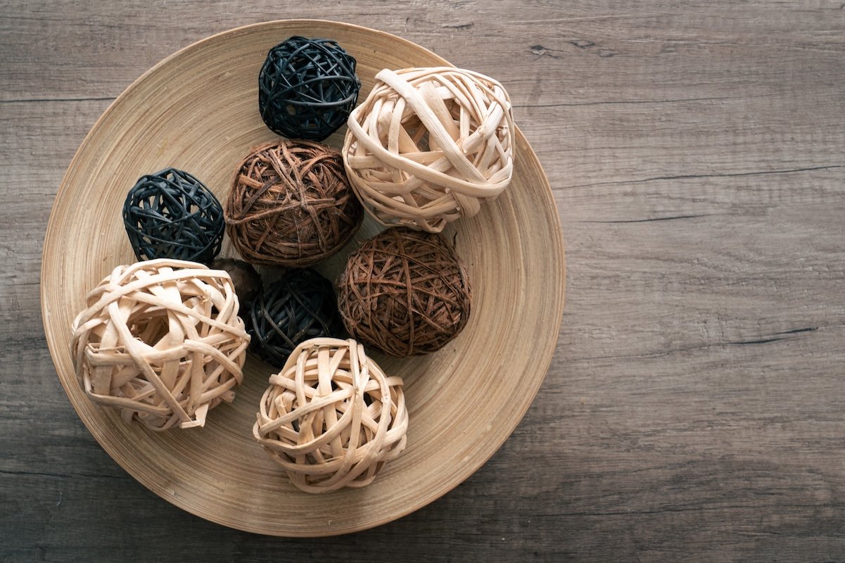 A wood bowl full of natural-colored decorative wicker balls of various sizes.