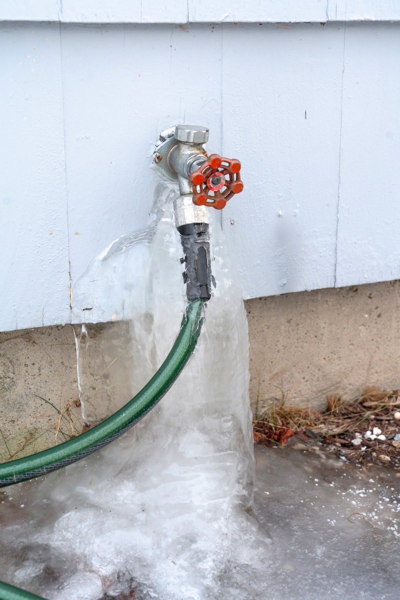 A frozen leaking outdoor spigot on the side of a house.
