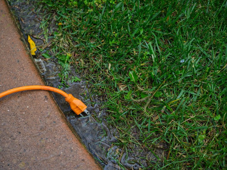 An extension cord in a puddle of standing water in a yard.
